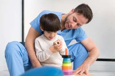 young therapist helping cute little boy who has cerebral palsy playing with developing toy