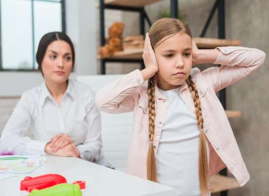 photo close-up of female psychologist looking at annoyed girl covering her ears with two hands