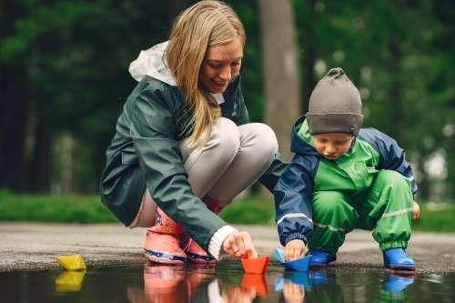 child and caretaker playing outside with a puddle and trying to float toys on it