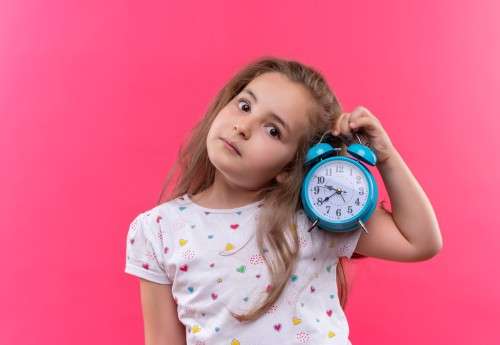 young girl holding an alarm clock and tilting her head