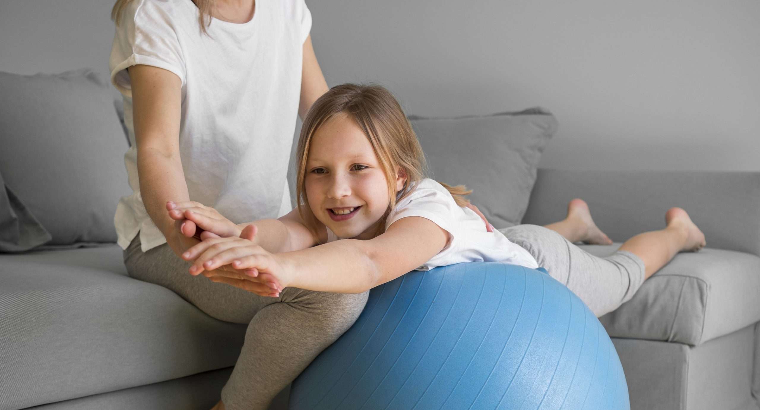 Mom helping girl to exercise on ball
